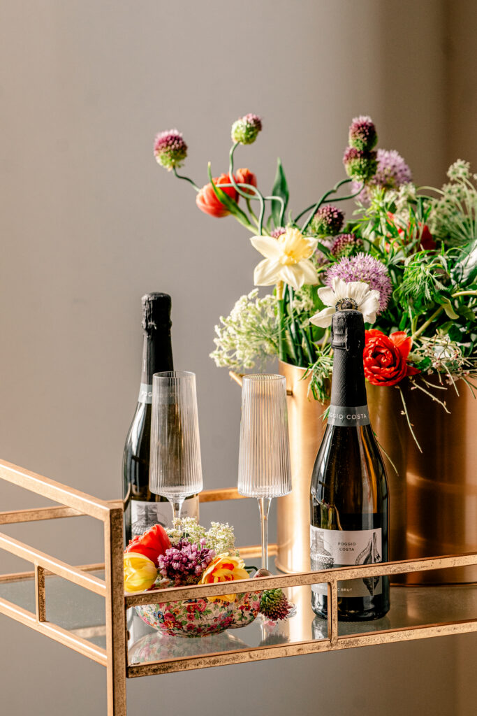 A gold bar cart with champagne and flowers for decoration at a tea party wedding