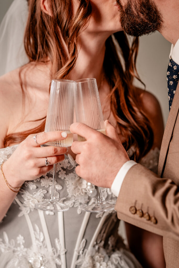 A bride and groom sharing a kiss as they clink champagne glasses for their Catholic wedding photographer