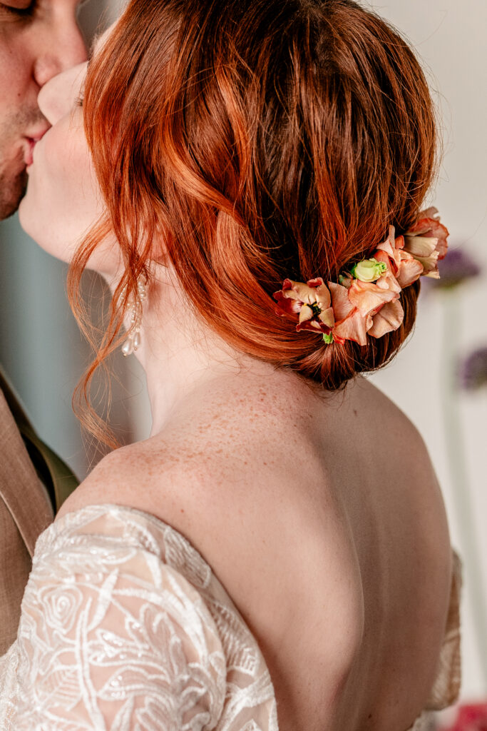 A close up of a bride with red hair with flowers tucked into her bun