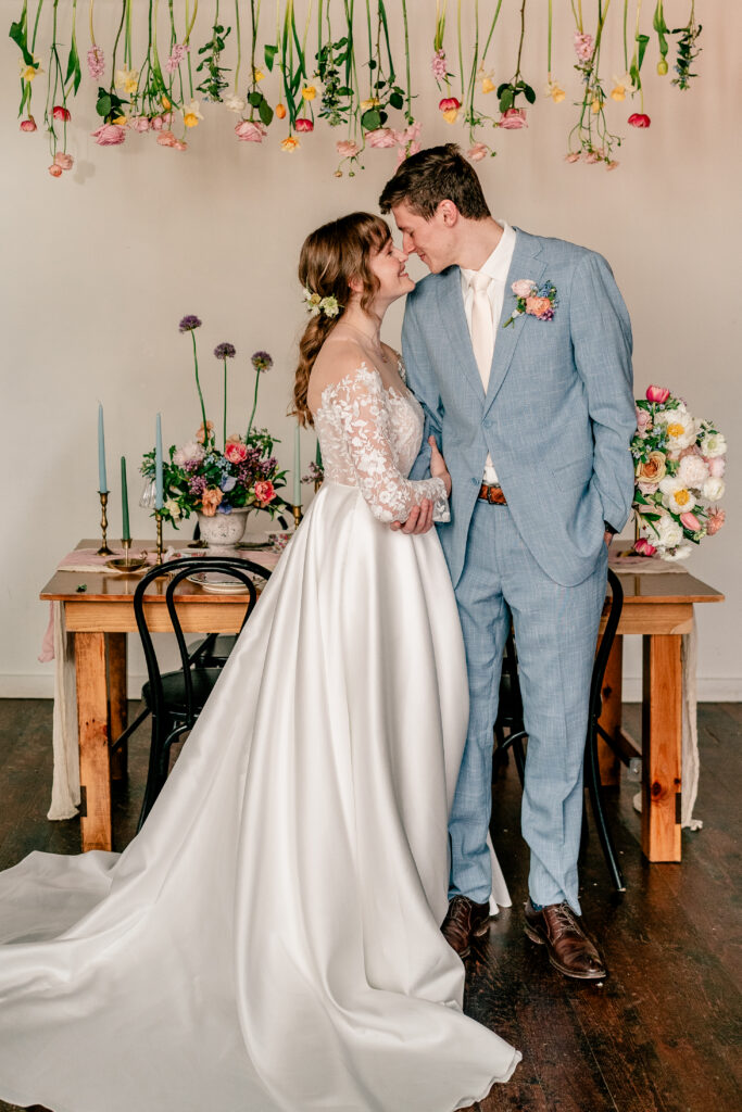 A bride and groom posing nose to nose in front of their floral sweetheart table