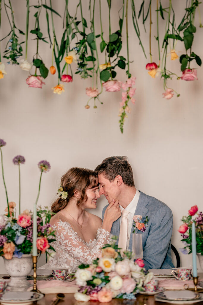 A bride and groom sharing a sweet moment at their sweetheart table with flowers hanging overhead with their Catholic wedding photographer
