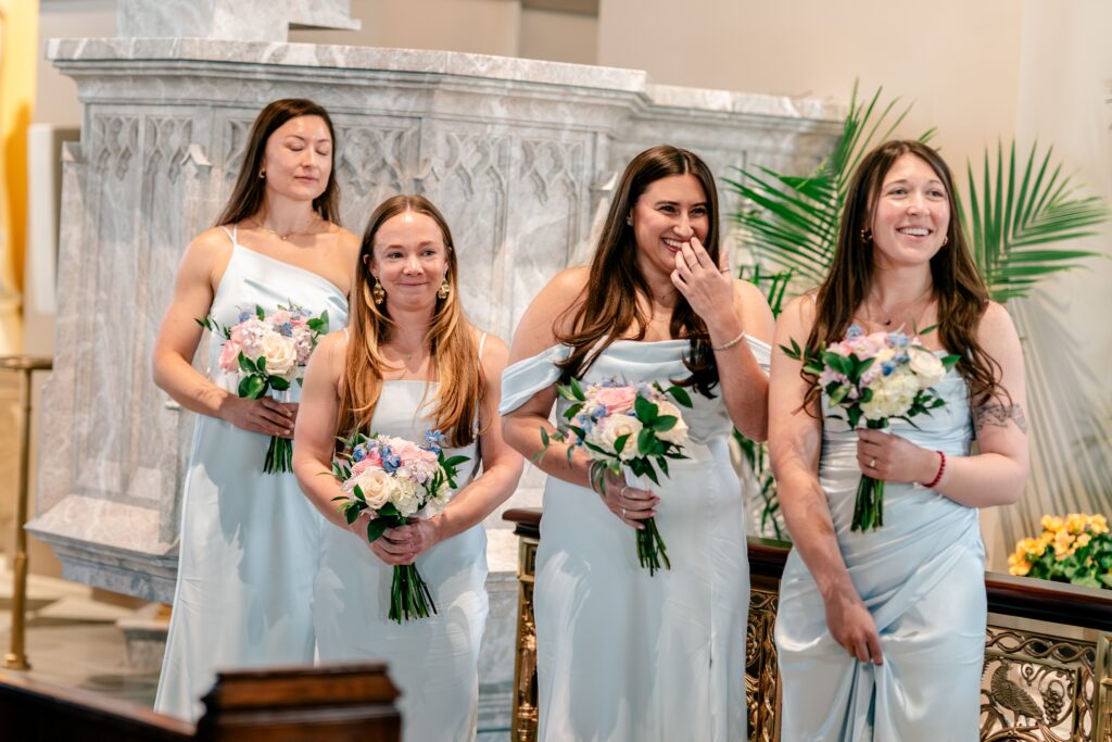 Bridesmaids laughing and holding back tears as they see the bride entering her ceremony