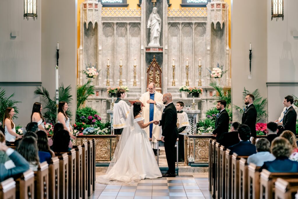 A bride and groom standing at the altar surrounded by their wedding party before saying their vows