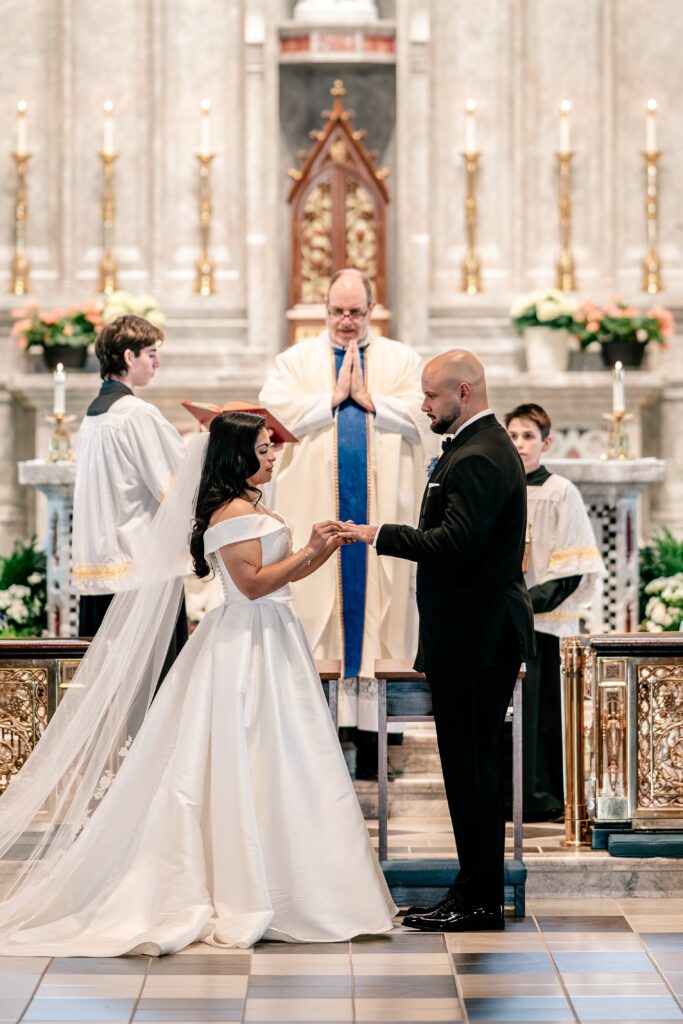 A bride putting the ring on her new husband's finger during their wedding at Corpus Christi Catholic Church in Aldie, VA