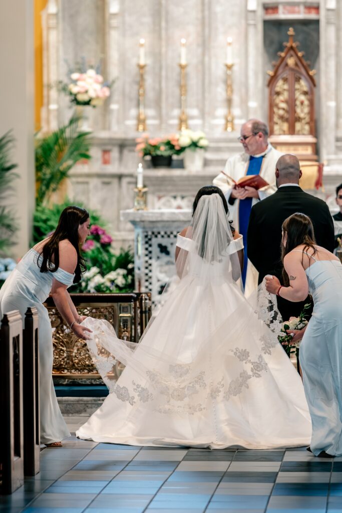 A pair of bridesmaids straightening the bride's cathedral veil during her ceremony
