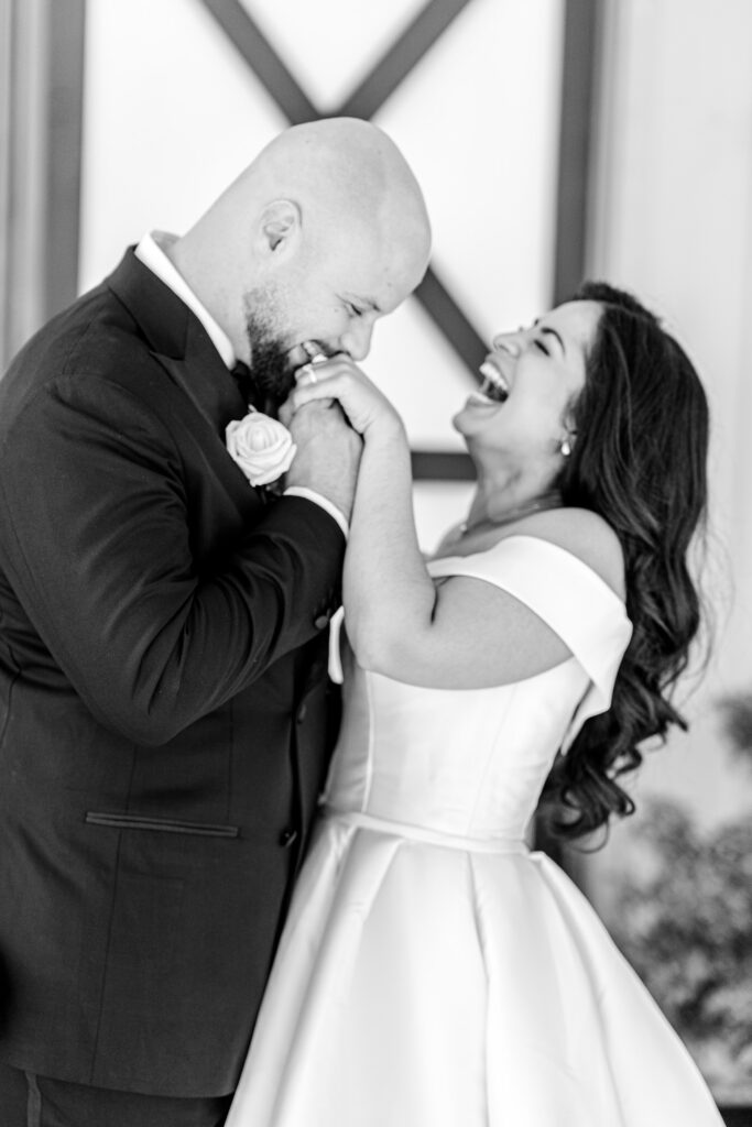 A groom kissing the hand of the bride as she laughs during their portraits for a Shadow Creek wedding