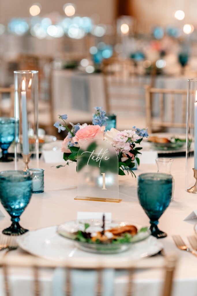 A close up of a reception table featuring blue water goblets and frosted table numbers during a Shadow Creek wedding