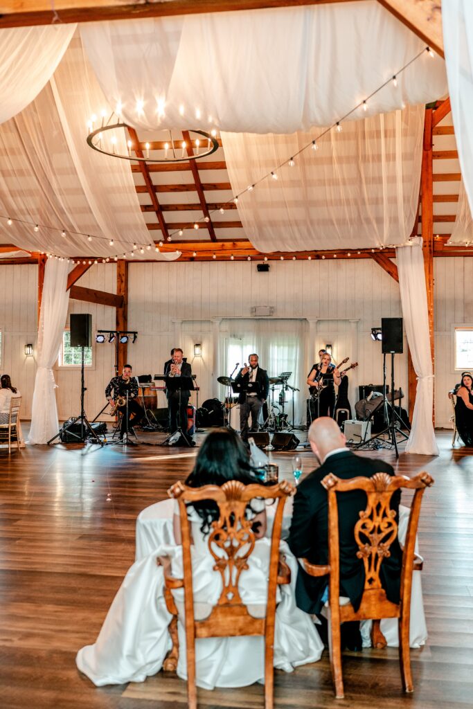 A bride and groom seated across the dance floor from a band during a Shadow Creek wedding reception