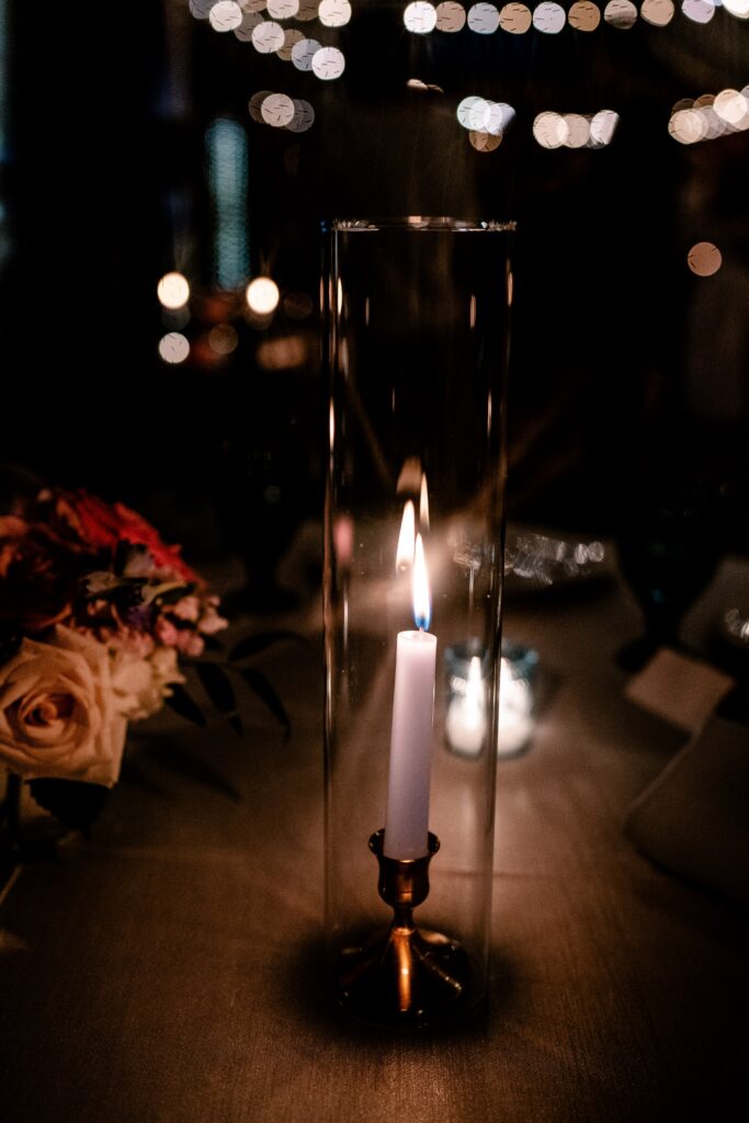 A taper candle glowing in the dark at a wedding reception